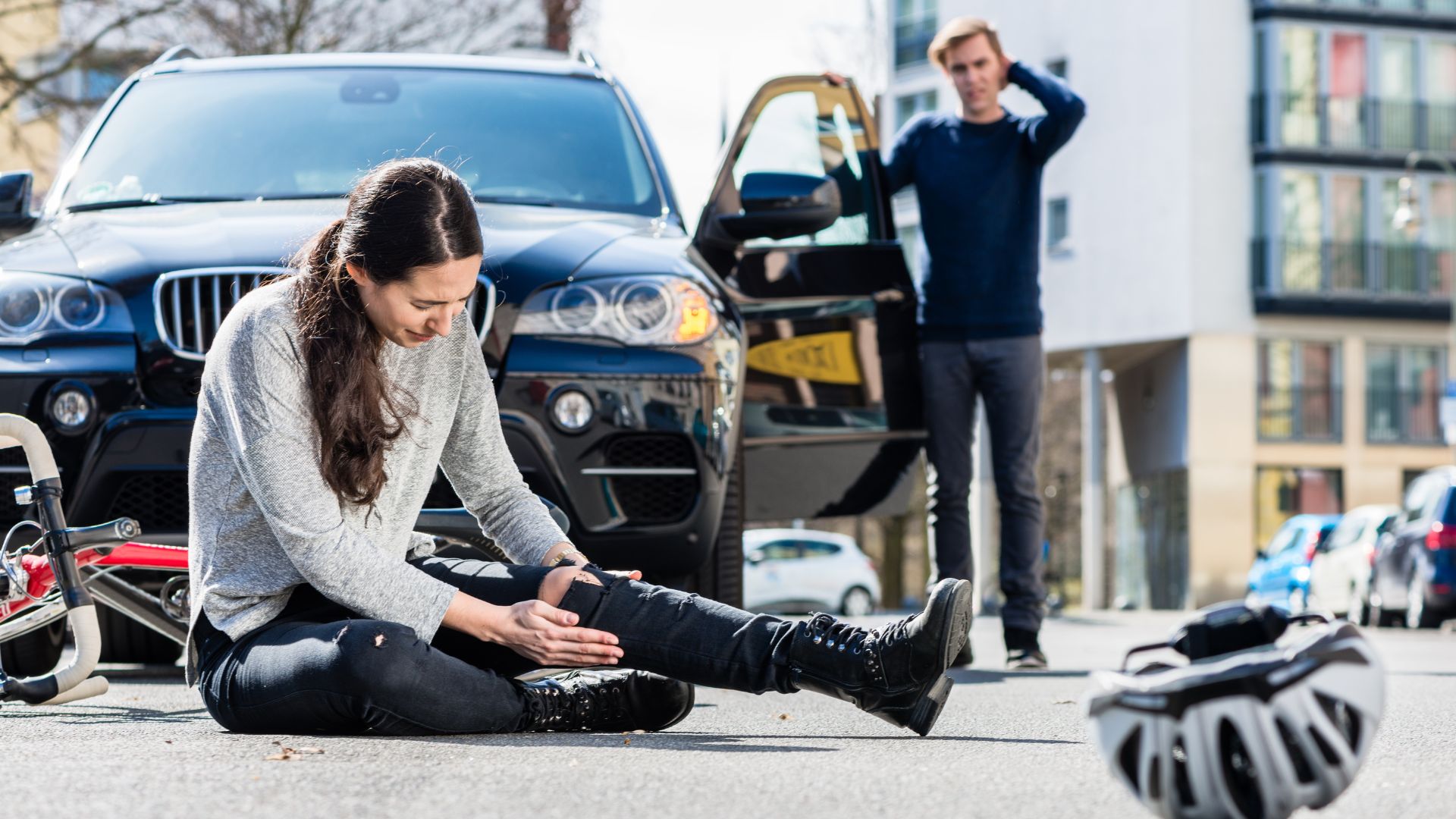 a woman on the ground holding her leg because she got hit on her bicycle and was hit by a car